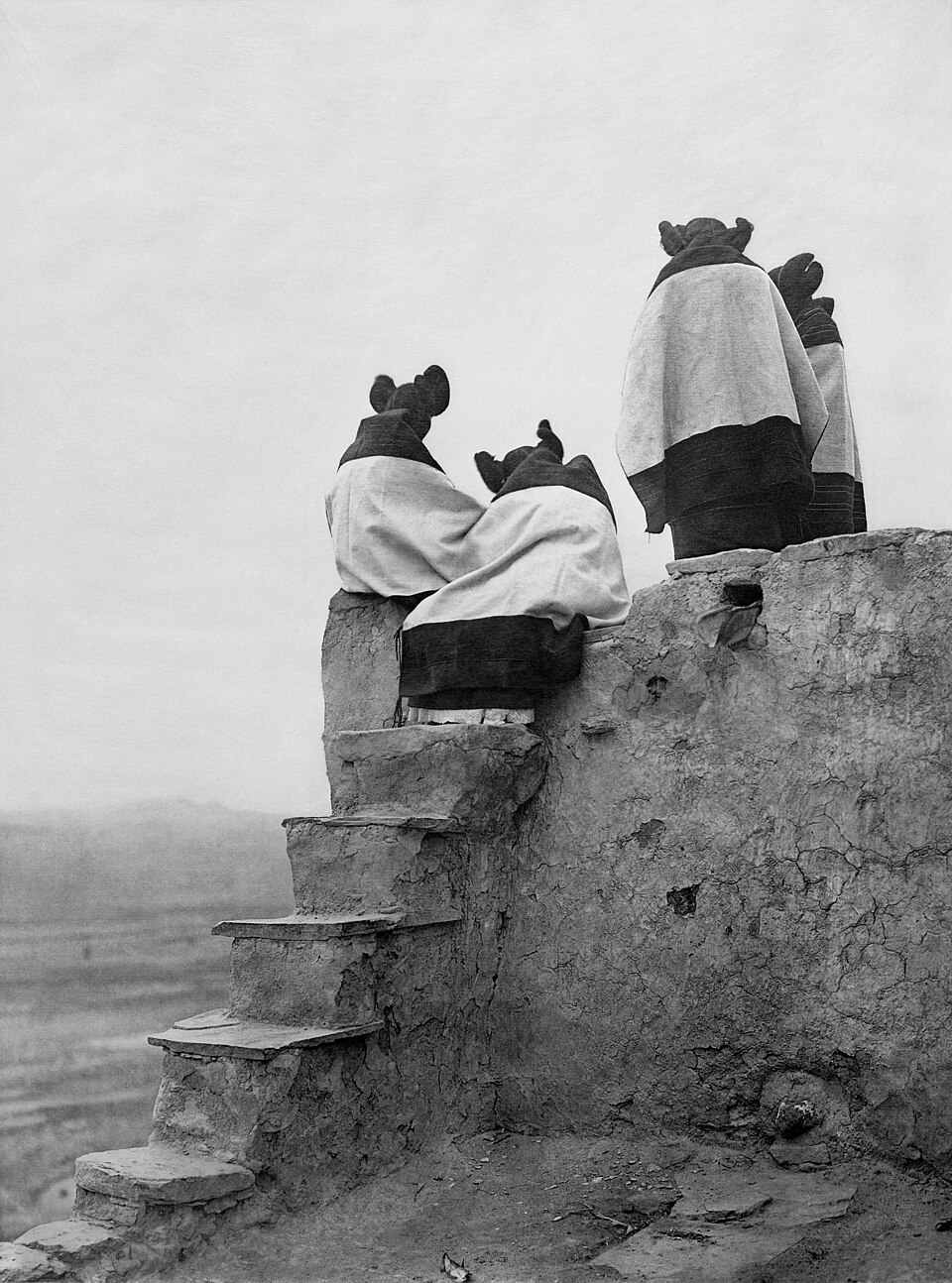 A group of girls on the topmost roof of Walpi Pueblo, looking down into the plaza.